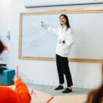 Smiling teacher instructing students in a classroom setting using a whiteboard.
