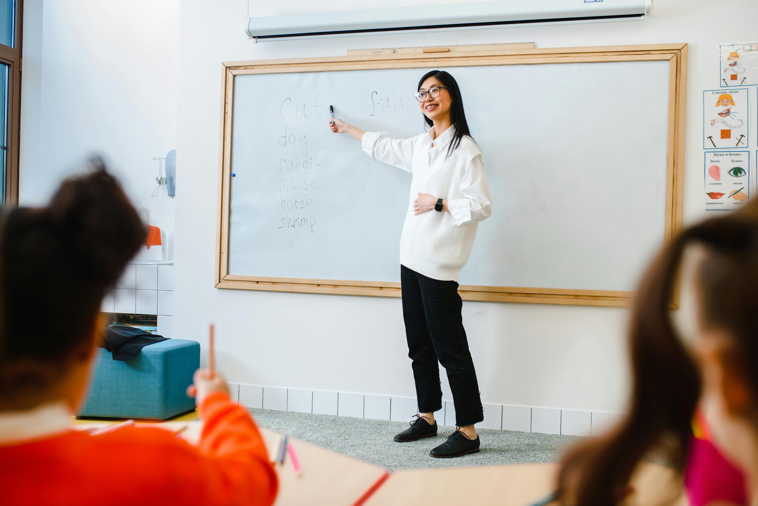 Smiling teacher instructing students in a classroom setting using a whiteboard.